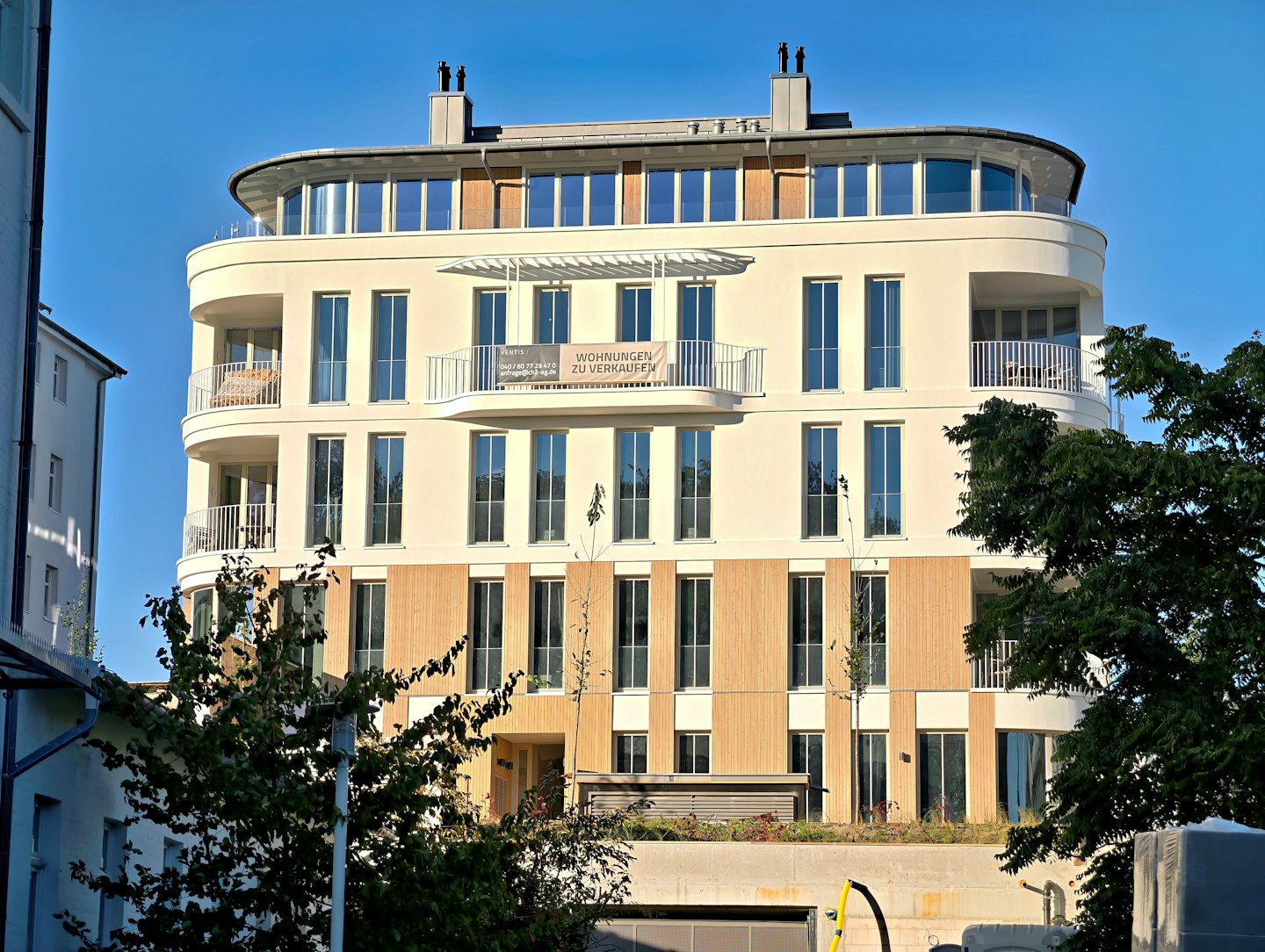 Nowoczesny budynek apartamentowy z zaokrąglonymi balkonami i banerem "na sprzedaż".