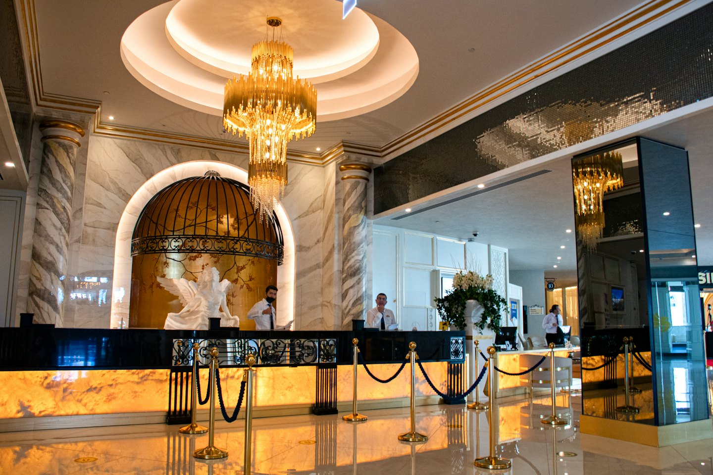 Dwóch mężczyzn za recepcją hotelową ze złotymi akcentami.