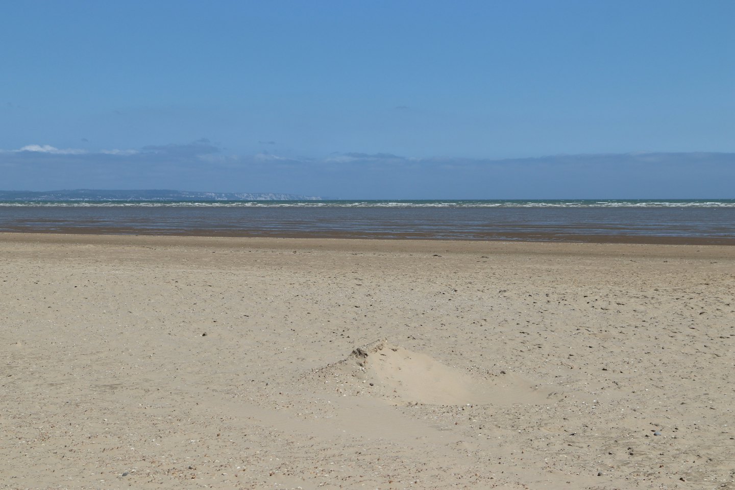 Piaszczysta plaża ciągnie się w stronę spokojnego, błękitnego morza.